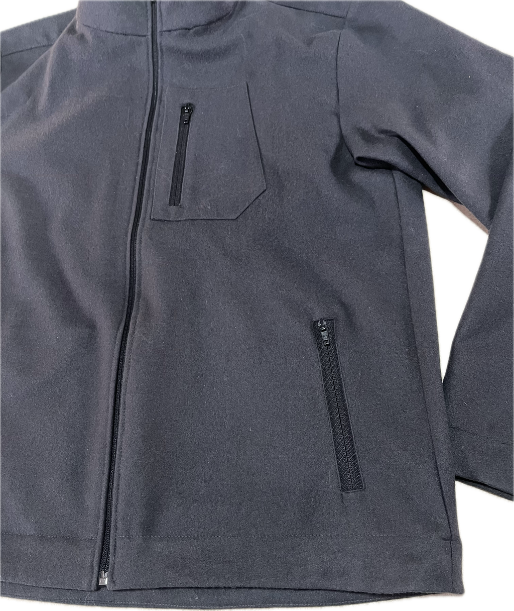 Roughstuff Leichtgaist leichte Lodenjacke für Alltag, Wandern und Outdoor-Aktivitäten. Dünne und angenehm zu tragende Jacke aus robuster Wollmischung mit sportlichem Schnitt, verstellbarem Bund und hoher Bewegungsfreiheit durch Rückenfalten. Ausgestattet mit seitlichen Taschen und Brusttasche, ideal als Zwischenschicht oder leichte Außenschicht bei mildem Wetter. Detail Tasche Farbe Anthrazit