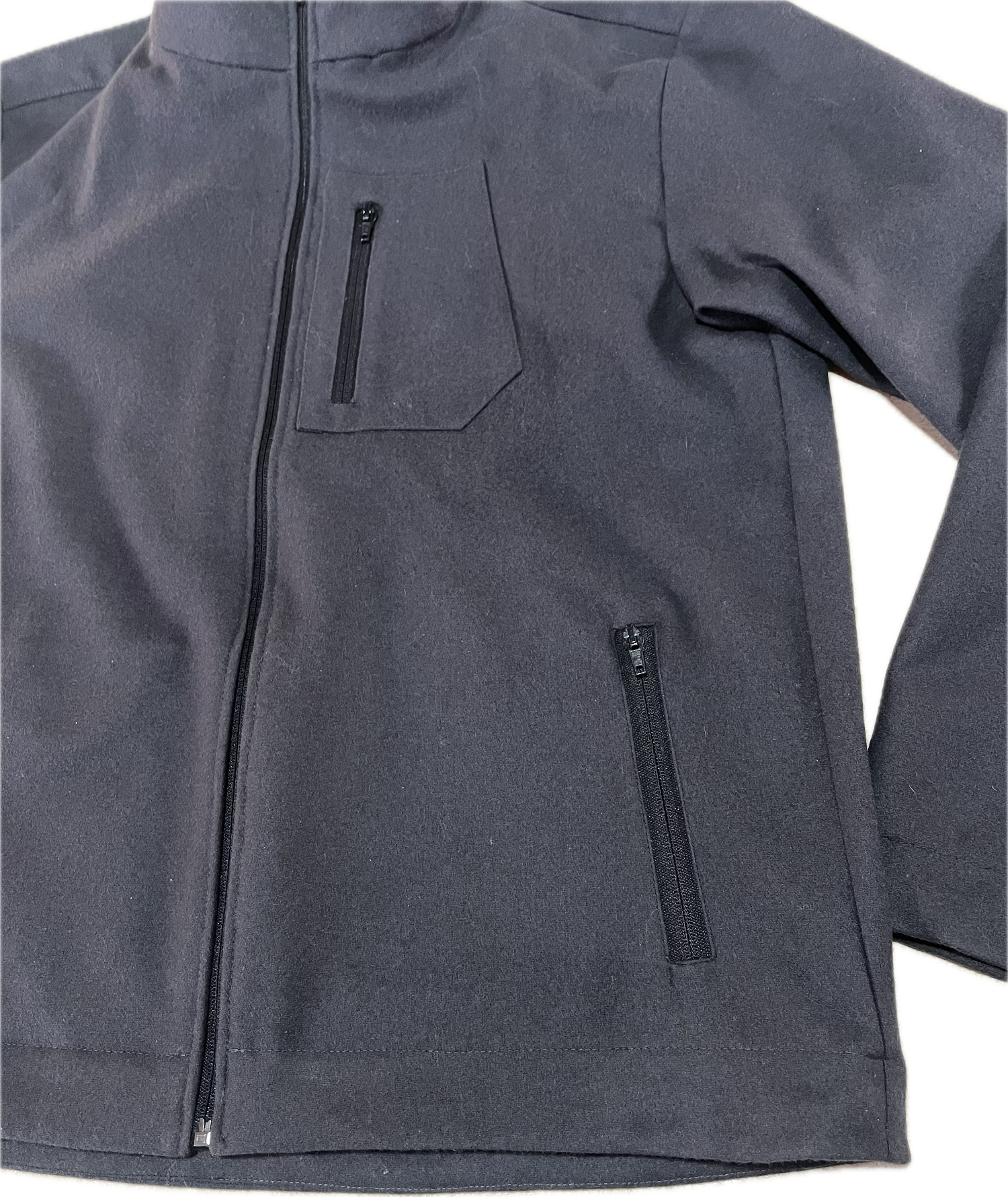 Roughstuff Leichtgaist leichte Lodenjacke für Alltag, Wandern und Outdoor-Aktivitäten. Dünne und angenehm zu tragende Jacke aus robuster Wollmischung mit sportlichem Schnitt, verstellbarem Bund und hoher Bewegungsfreiheit durch Rückenfalten. Ausgestattet mit seitlichen Taschen und Brusttasche, ideal als Zwischenschicht oder leichte Außenschicht bei mildem Wetter. Detail Tasche Farbe Anthrazit