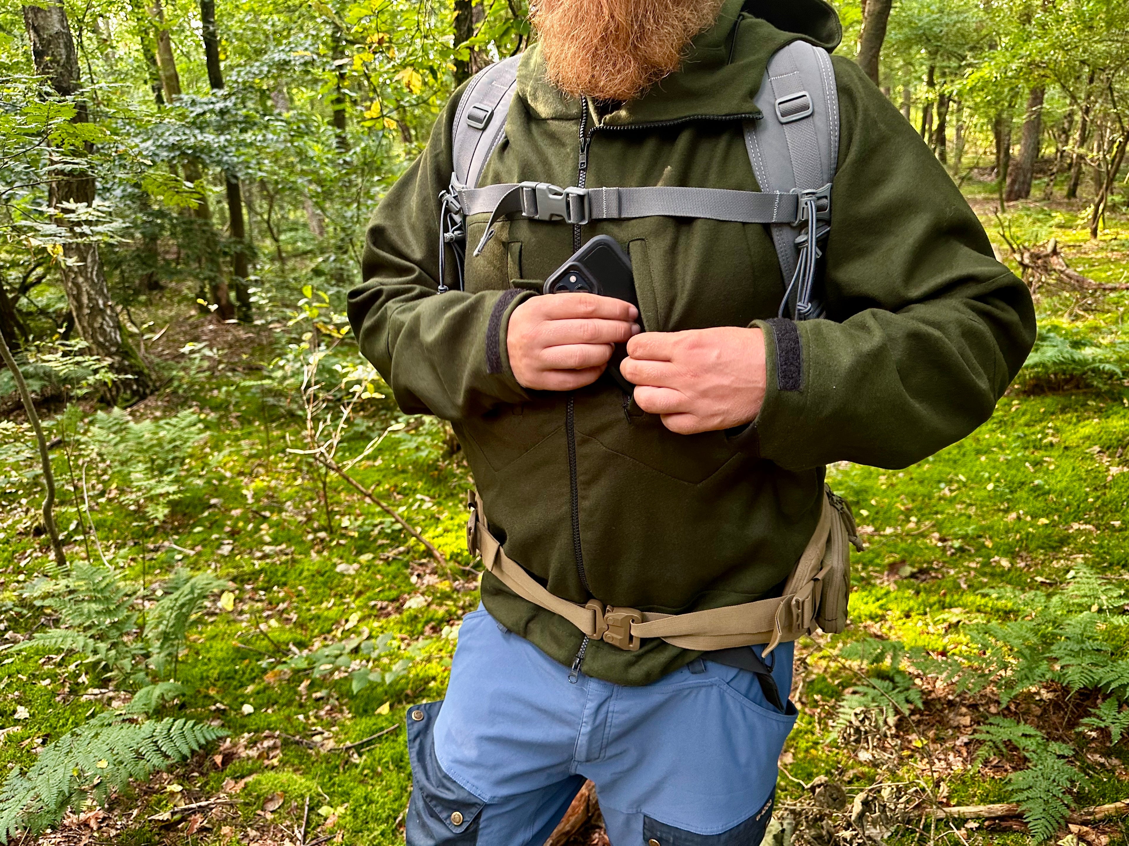 Roughstuff Bergteufel technische Lodenjacke für Outdoor, Trekking und Abenteuer bei jedem Wetter. Robuste Outdoorjacke mit sportlichem Schnitt, großer verstellbarer Kapuze, hohem Kragen und langen Belüftungsreißverschlüssen für optimalen Wind- und Wetterschutz. Ausgestattet mit großen Taschen, Raglanärmeln und funktionalen Details für maximale Bewegungsfreiheit beim Wandern, Radfahren und Bushcraft. Farbe Olivgrün Detail Brust Tasche